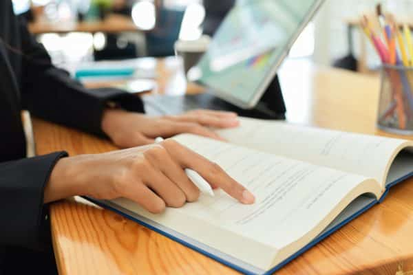 Close up of a person reading a book at a desk.